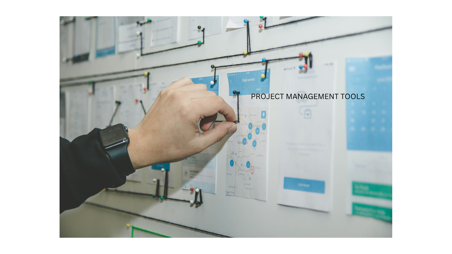  A person's hand pointing at a physical project board filled with colorful notes,documents,and a the prhase "project management tools."